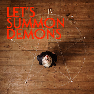 Picture taken from above of a woman standing on a pentacle chalked onto a wooden floor. The words read 'Let's Summon Demons'.