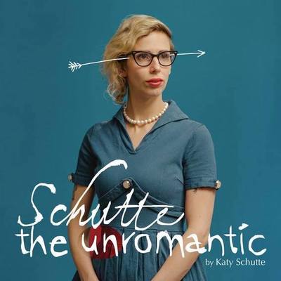 A blue background with a portrait of a woman in the foreground wearing a similarly blue 50s style dress. She is wearing cateye glasses and red lipstick. There is an arrow drawn on in white that goes through her head. The title says 'Schutte the Unromantic by Katy Schutte'.